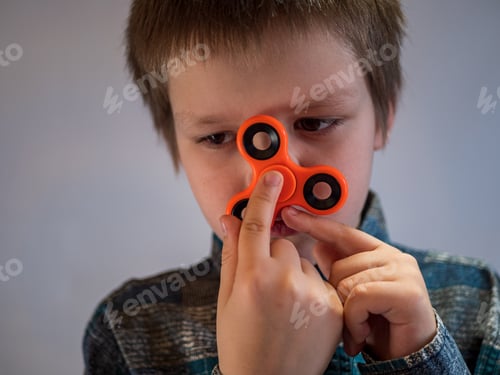 Preview: Funny Blond Child In Colored Shirt Twists Spinner On His Nose. Portrait Of Boy On White Background