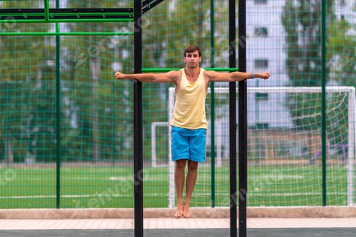 Preview: Strong Muscular Athletic Young Man Hanging Suspended From Nets At An Outdoor Gym With Straight