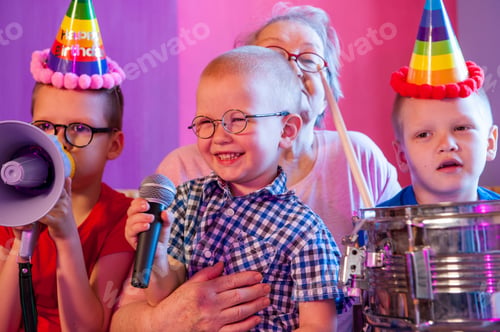 Preview: Elderly Woman In Pink T-Shirt And Glasses Holding Megaphone. Next To Grandmother, Grandchildren In