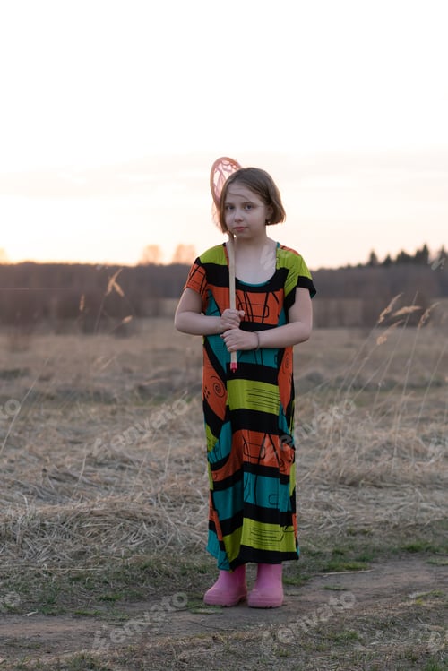 Preview: Little Scandinavian Girl In A Field In Spring With A Net Stands In A Colored Dress