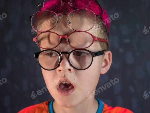 Preview: Photo Of Funny Boy, Blonde Kid With Lot Of Pairs Of Glasses On His Face. Child Is Happy At Home On