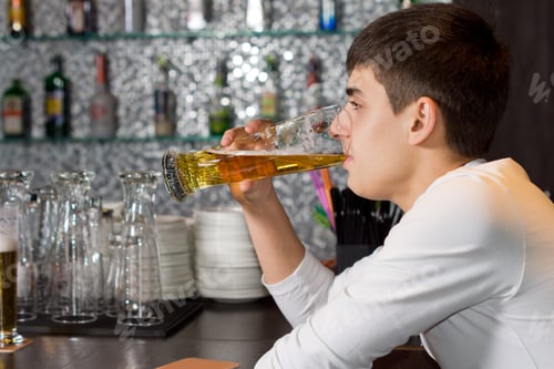 Preview: Close Up Side View Of A Young Man Drinking A Pint Of Draught Beer While Sitting At The Counter In A