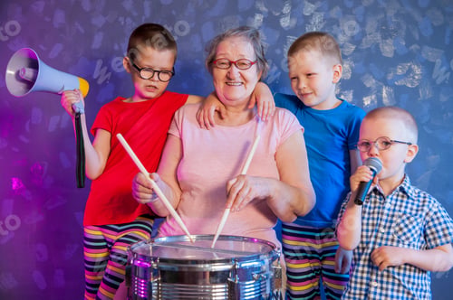 Preview: Elderly Woman In Pink T-Shirt And Glasses Holding Megaphone. Next To Grandmother, Grandchildren In