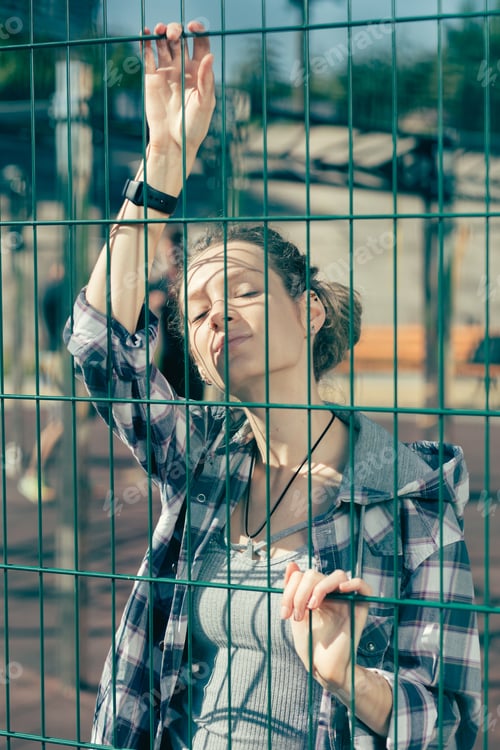 Preview: Calm Beautiful Woman Touching The Chain Link Fence While Standing On The Sports Ground Alone