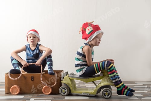 Preview: Two Funny Boys In Santa Claus Hat And Striped Clothes Are Playing With Plywood Box Clinging To Toy