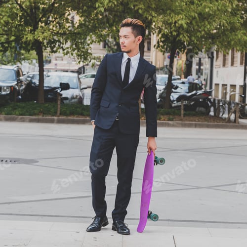 Preview: Young Handsome Asian Model Dressed In Dark Suit And Tie Posing With His Skateboard