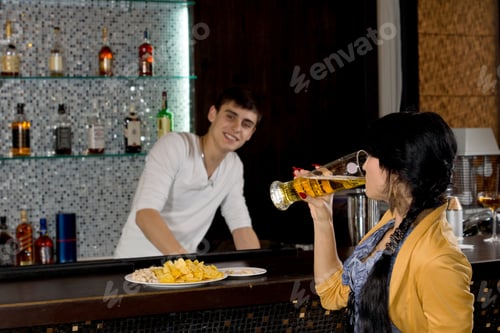 Preview: Side View Of A Young Woman Drinking A Pint Of Beer In A Nightclub With A Smiling Friendly Bartender