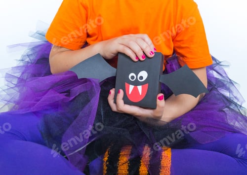 Preview: A Little Girl In A Witch Costume Holds A Bat. Halloween Party. Hand Made Gift Wrapping.