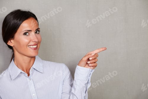 Preview: Long Hair Female Pointing To Her Left And Smiling In Formal Clothing While Looking At Camera On
