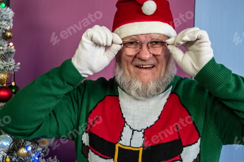 Preview: Elderly Man With Gray Beard And Glasses In Santa Claus Hat With Red Bag Filled With Presents Poses