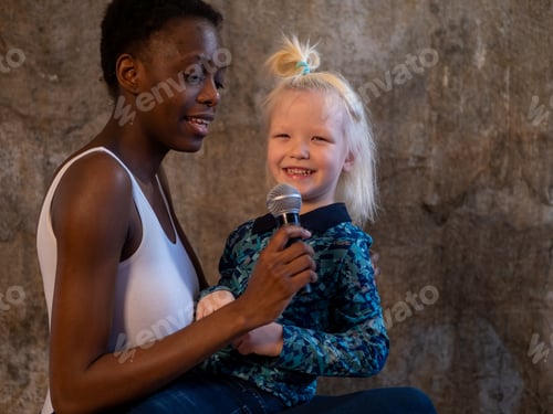 Preview: African American Woman In White Bodysuit And Jeans And Caucasian Blond Boy Sing Karaoke With