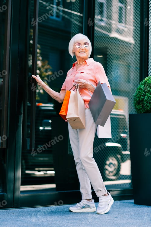 Preview: Happy Aged Woman Touching Door Handle And Smiling While Having Shopping Bags In Hand