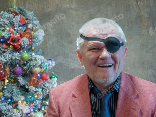 Preview: Elderly Hipster Man In Pink Jacket And Black Bandage Through One Eye Sits On Background Of