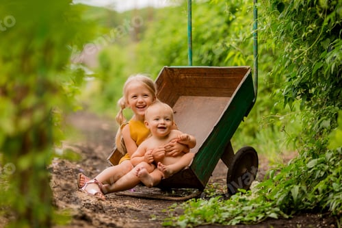 Preview: Two Small Children Girl And Boy In The Country In A Garden Wheelbarrow Sitting Smiling