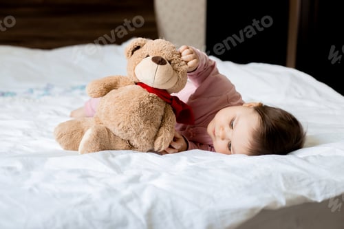 Preview: Portrait Of A Toddler Girl Smiling, Lying On A Bed With A Teddy Bear. Space For Text