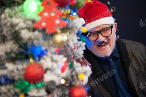 Preview: Elderly Man In Glasses With Gray Hair And Beard Next To Luminous And Blinking Christmas Lights