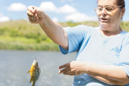 Preview: Middle Aged Woman Holding Up A Fish Dangling From The End Of A Fishing Line As She Fishes On A