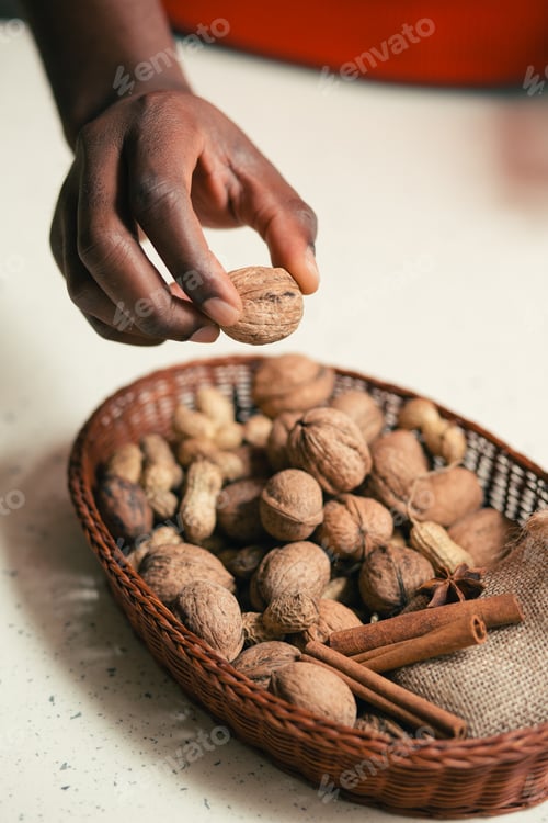 Preview: Hand Of Man Holding A Walnut Above The Wicker Basket With Cinnamon And Nuts In It