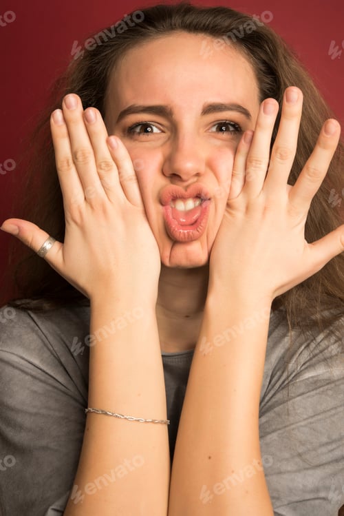 Preview: Beautiful Brunette Female Making Funny Faces And Posing In Studio Isolated On Red Background