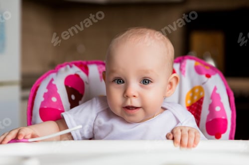 Preview: Baby In The Kitchen In A Baby Chair Holding A Spoon And Smiling.Sweet Baby In High Chair.Cheerful