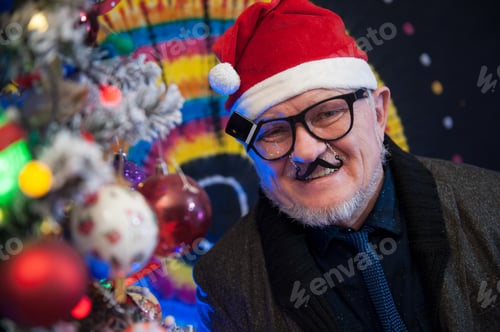 Preview: Elderly Man In Carnival Glasses With Gray Hair And Beard Next To Luminous And Blinking Christmas