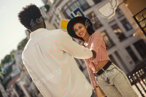 Preview: Cheerful Young Woman In Stylish Summer Clothes Gently Pulling A Hand Of Her Boyfriend And Smiling