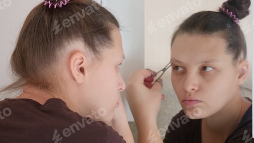 Preview: Pretty Girl With Tweezers Plucks Her Eyebrows In Front Of Mirror. Cosmetic Procedures. Close-Up
