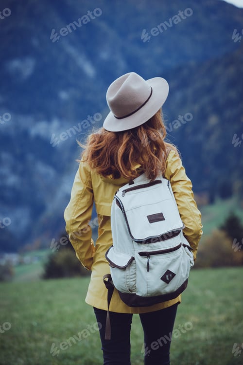 Preview: Girl In The Hat With A Backpack Stands On The Meadow In The Mountain