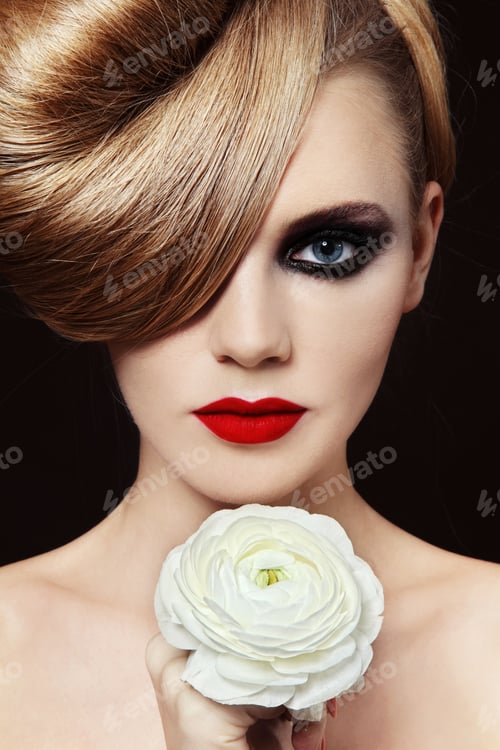 Preview: Young Beautiful Woman With Fancy Hairdo And Smoky Eyes Holding White Flower In Her Hand