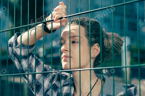 Preview: Close Up Of Young Lady With Dreadlocks Thoughtfully Looking Through The Chain Link Fence