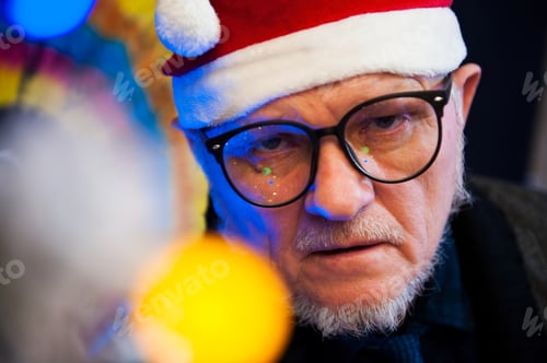 Preview: Elderly Man In Glasses With Gray Hair And Beard Next To Luminous And Blinking Christmas Lights