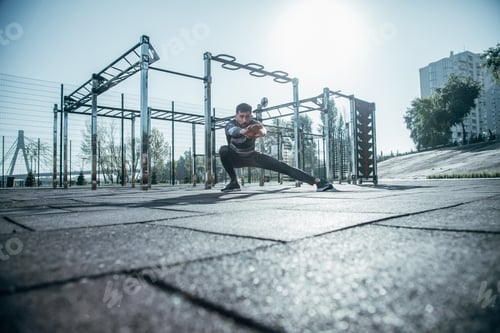 Preview: Concentrated Young Man In Sports Clothes Sitting Down And Doing Stretching Exercises While Being At
