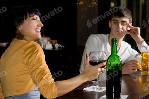 Preview: Optimistic Young Brunette Woman Drinking Red Wine At The Bar Next To Her Pessimistic Male Friend