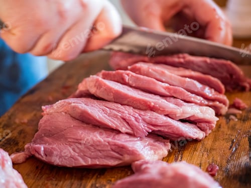 Preview: Beautiful Mature Woman In Pink Sweater And Gray Economic Apron Cuts Large Piece Of Pork Into Pieces