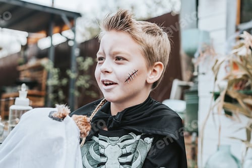 Preview: A Boy In A Skeleton Costume With A Dog In A Ghost Costume On The Porch Of A House Decorated To