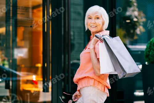 Preview: Mirthful Aged Woman With Paper Bags Smiling When Standing Near The Shop