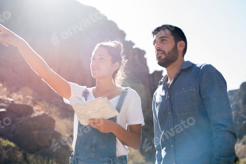 Preview: Couple Standing On A Mountain Path Pointing At The Horizon As The Woman Holds A Map
