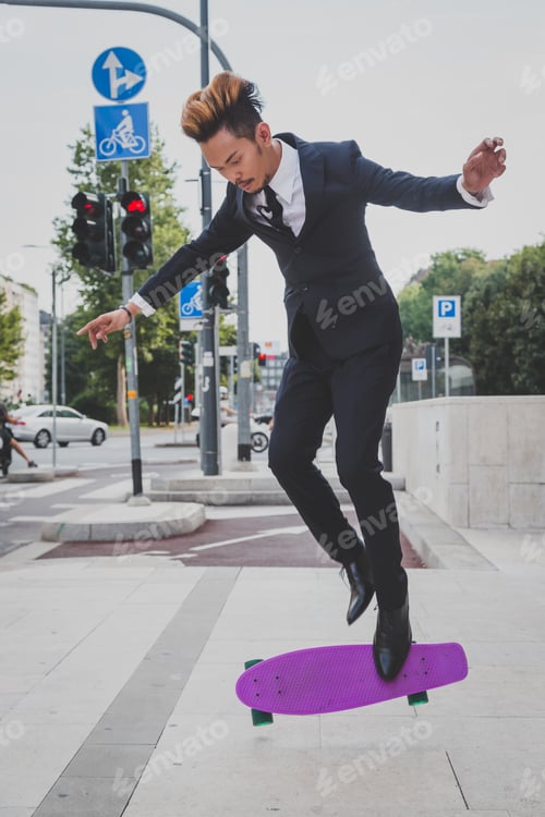Preview: Young Handsome Asian Model Dressed In Dark Suit And Tie Jumping With His Skateboard