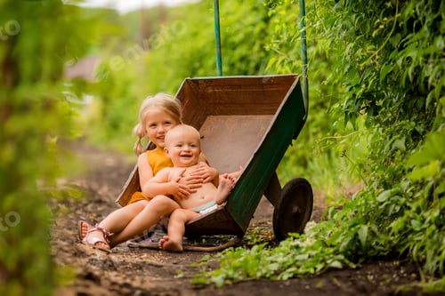 Preview: Two Small Children Girl And Boy In The Country In A Garden Wheelbarrow Sitting Smiling