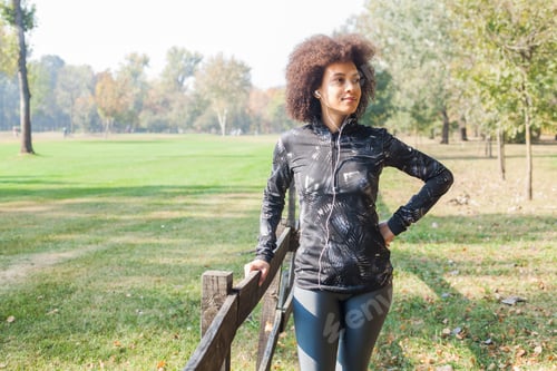 Preview: Attractive Sporty Woman Relax After Training Listening Music At Park, Leaning On Wooden Fence In