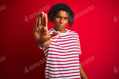 Preview: Young Afro Man With Dreadlocks Wearing Striped T-Shirt Standing Over Isolated Red Background Doing