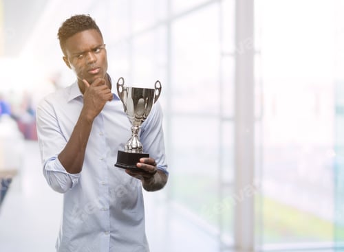 Preview: Young African American Man Holding Trophy Serious Face Thinking About Question, Very Confused Idea