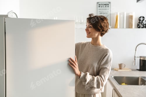 Preview: Happy Young Woman Standing At The Opened Fridge