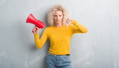Preview: Young Blonde Woman Over Grunge Grey Background Holding Megaphone With Angry Face, Negative Sign
