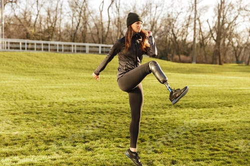 Preview: Image Of Happy Handicapped Woman 20S In Tracksuit Doing Sports On Nature And Raising Prosthesis Leg
