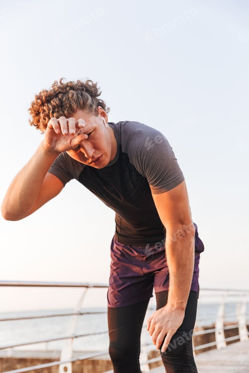 Preview: Portrait Of A Sweaty Sportsman Resting After Workout At The Beach, Listening To Music With Earphones