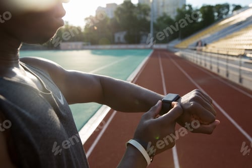 Preview: Cropped Image Of A Young African Athlete Using Wrist Smartwatch At The Stadium