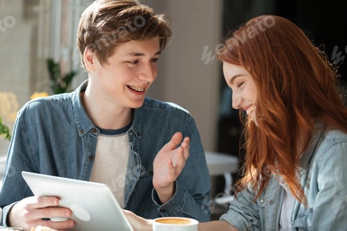 Preview: Young Smiling Couple Talking While Using Tablet In Cafe