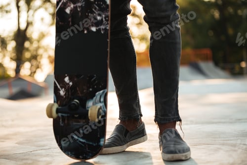 Preview: Cropped Image Of An African Man Skateboarder Standing With A Skateboard At A City Park