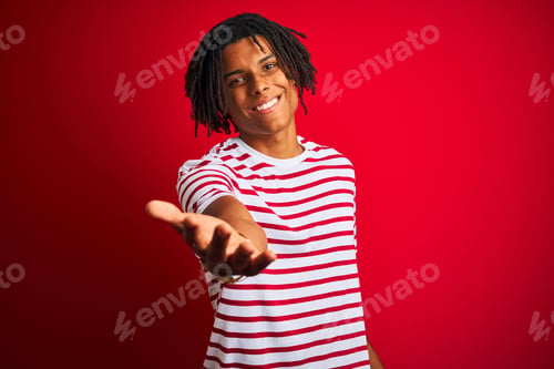 Preview: Young Afro Man With Dreadlocks Wearing Striped T-Shirt Standing Over Isolated Red Background